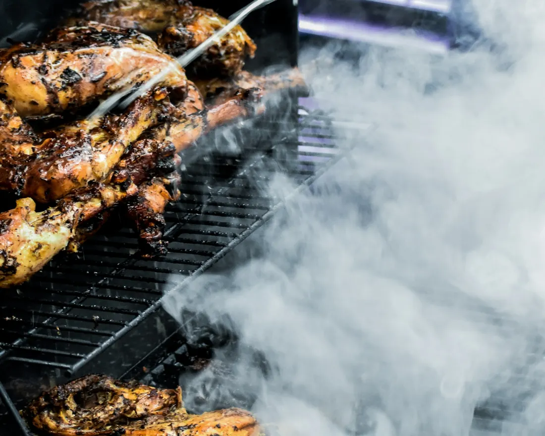 Looking through the kitchen window at jerk chicken smoking on the grill